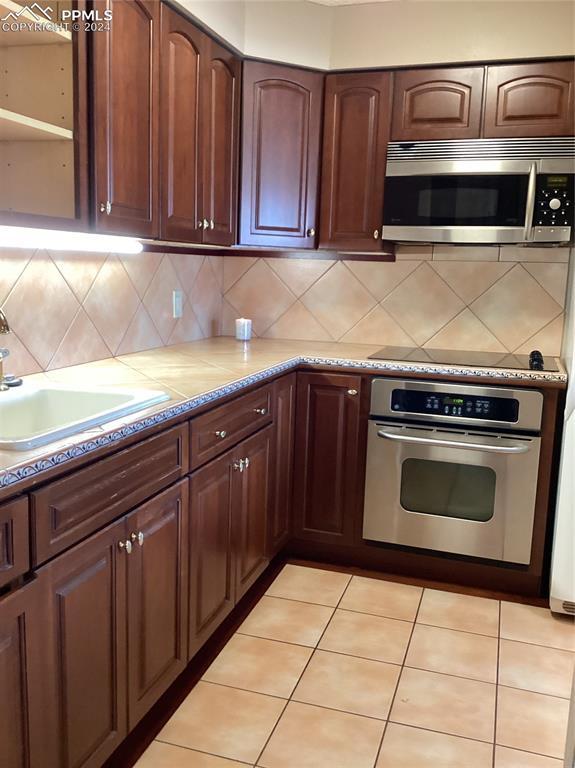 kitchen with light tile patterned flooring, stainless steel appliances, tasteful backsplash, and sink