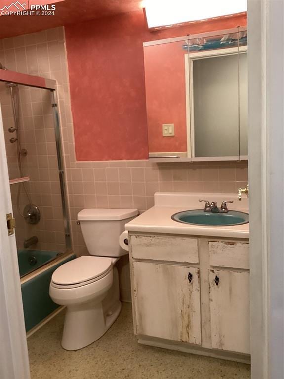 full bathroom with toilet, tile walls, vanity, and shower / bath combination with glass door