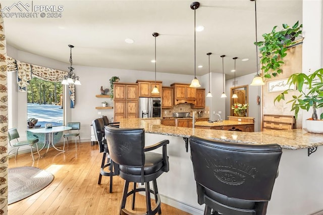 kitchen with hanging light fixtures, tasteful backsplash, light stone counters, kitchen peninsula, and stainless steel fridge