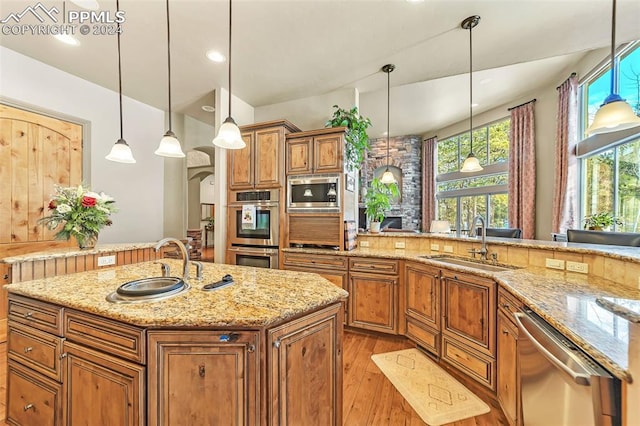 kitchen featuring sink, an island with sink, appliances with stainless steel finishes, decorative light fixtures, and light stone counters