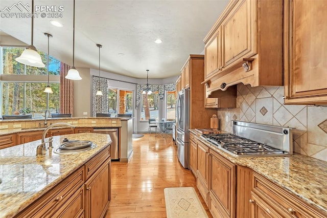 kitchen featuring backsplash, light wood-type flooring, decorative light fixtures, light stone counters, and stainless steel appliances