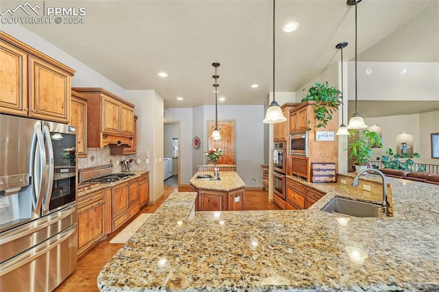 kitchen with light stone countertops, stainless steel appliances, a spacious island, sink, and pendant lighting