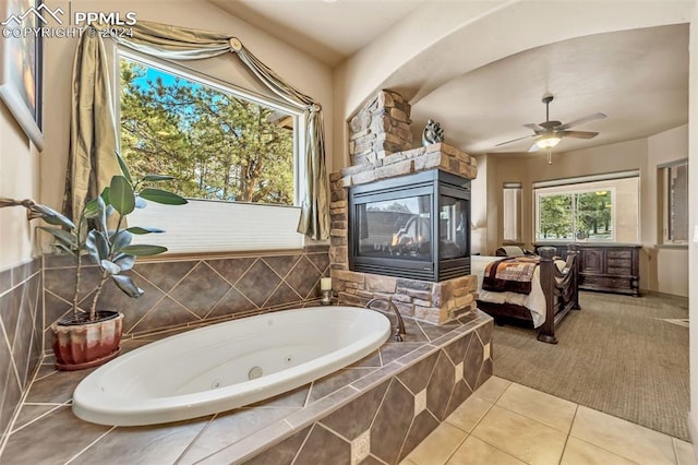 bathroom featuring tile patterned floors, a relaxing tiled tub, ceiling fan, and a multi sided fireplace