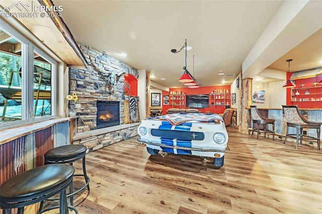 interior space with a stone fireplace, indoor bar, and light wood-type flooring