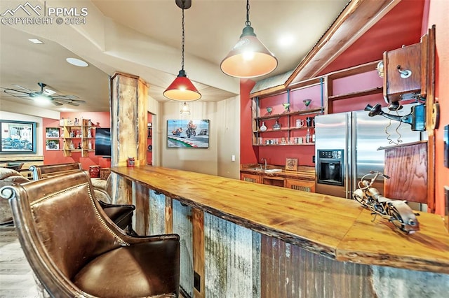 bar featuring decorative light fixtures, ceiling fan, wood counters, and stainless steel refrigerator with ice dispenser