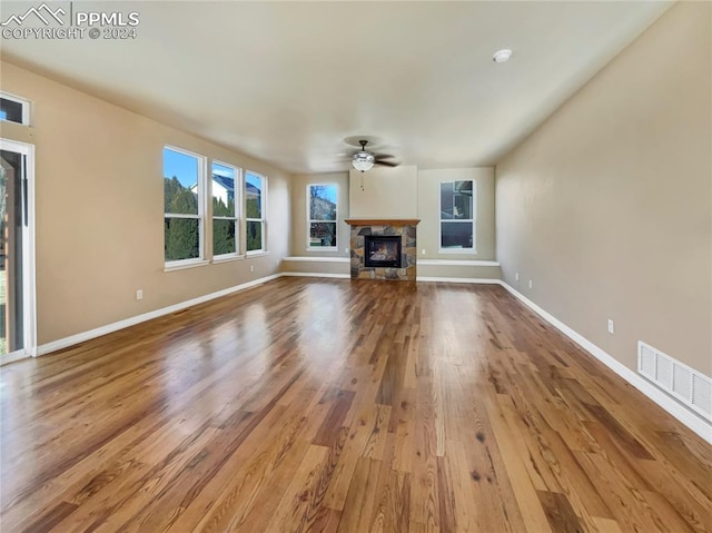 unfurnished living room with hardwood / wood-style floors, a stone fireplace, and ceiling fan