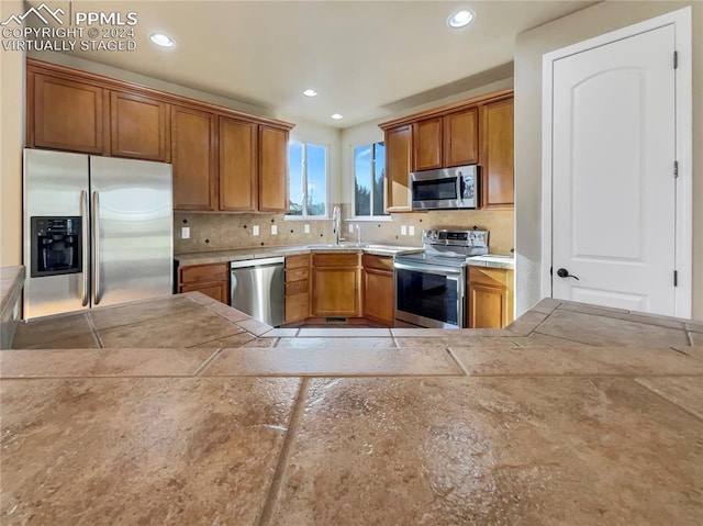 kitchen with tile countertops, decorative backsplash, sink, and stainless steel appliances