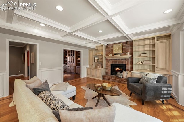 living room with a brick fireplace, coffered ceiling, ornamental molding, built in shelves, and beam ceiling