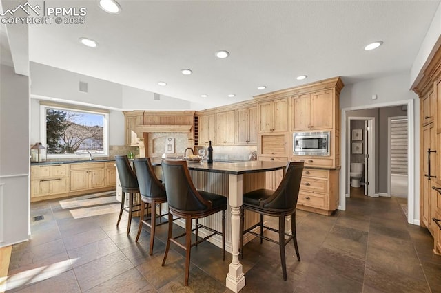 kitchen with decorative backsplash, light brown cabinets, stainless steel microwave, and an island with sink