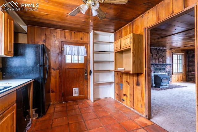 kitchen with a wood stove, ceiling fan, wood ceiling, wood walls, and black appliances