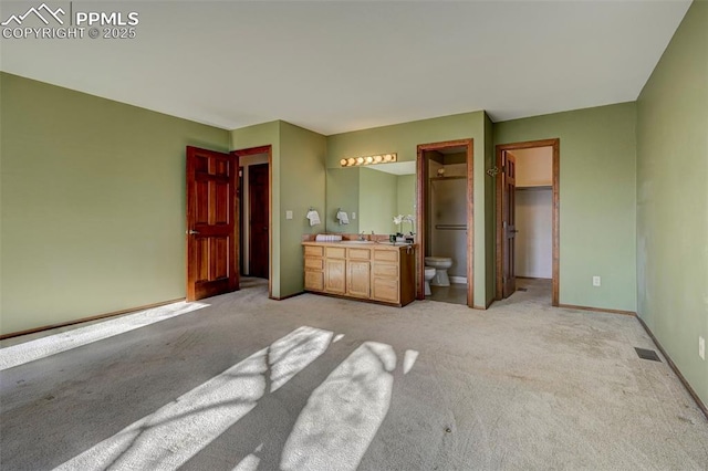 unfurnished bedroom with ensuite bathroom, light colored carpet, sink, a spacious closet, and a closet