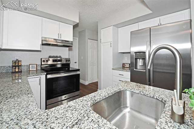 kitchen with white cabinetry, stainless steel appliances, light stone counters, and a textured ceiling