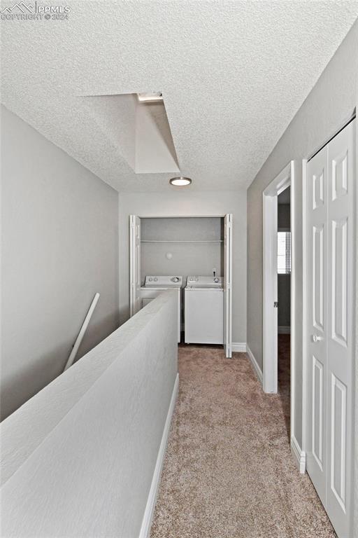 hallway with a textured ceiling, separate washer and dryer, and light colored carpet