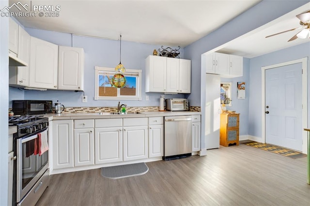 kitchen with appliances with stainless steel finishes, decorative light fixtures, white cabinetry, light hardwood / wood-style floors, and sink