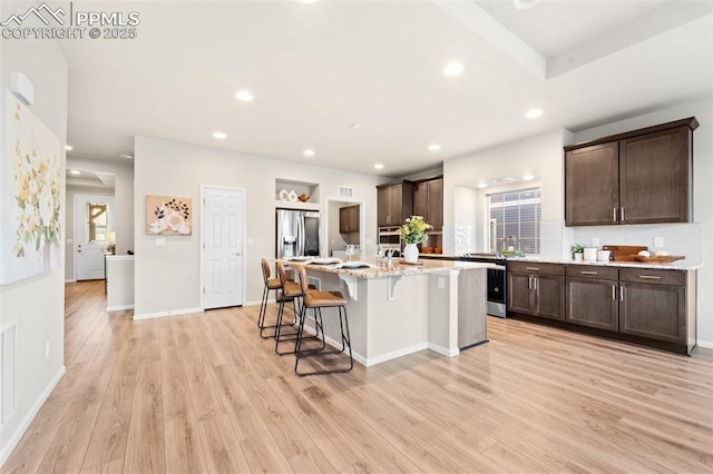 kitchen featuring light hardwood / wood-style flooring, stainless steel appliances, a center island, and a breakfast bar