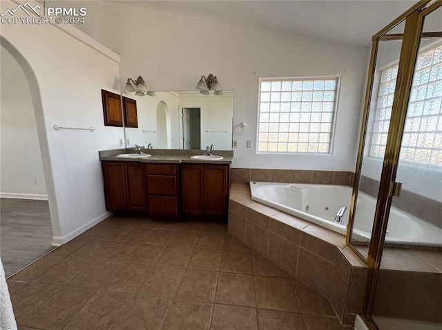 bathroom featuring vanity, vaulted ceiling, a relaxing tiled tub, and tile patterned floors