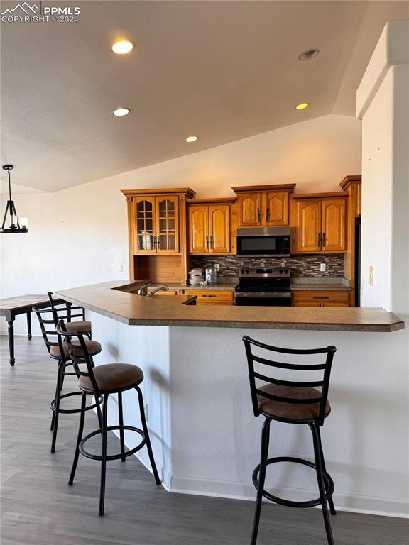 kitchen with a kitchen bar, hanging light fixtures, vaulted ceiling, and appliances with stainless steel finishes