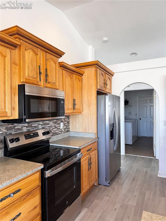 kitchen featuring lofted ceiling, tasteful backsplash, light hardwood / wood-style floors, stainless steel appliances, and washer / clothes dryer