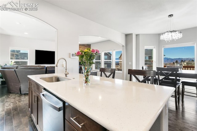 kitchen with pendant lighting, dishwasher, dark wood-type flooring, sink, and an island with sink