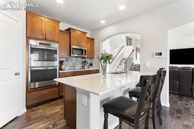 kitchen with a kitchen breakfast bar, sink, decorative backsplash, appliances with stainless steel finishes, and dark hardwood / wood-style flooring