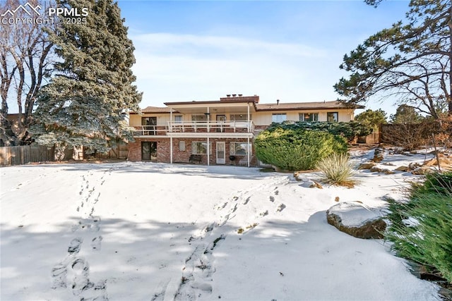 snow covered back of property featuring a balcony