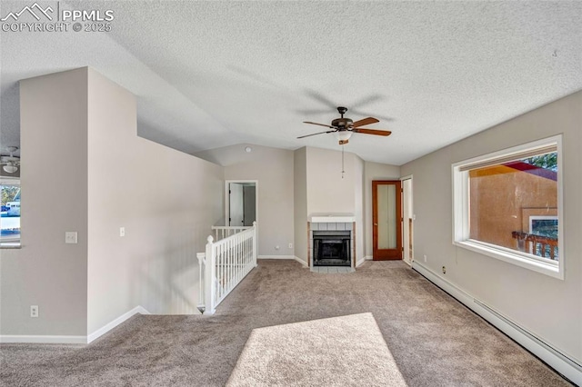 unfurnished living room with vaulted ceiling, light carpet, baseboard heating, a tile fireplace, and ceiling fan