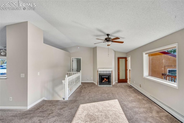 unfurnished living room featuring lofted ceiling, baseboard heating, ceiling fan, light colored carpet, and a tiled fireplace