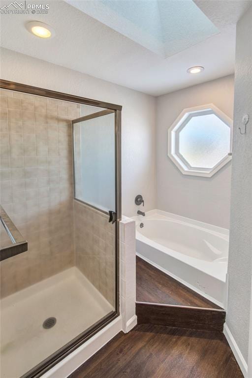 bathroom featuring shower with separate bathtub, a skylight, and hardwood / wood-style floors