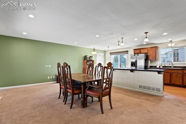 dining area with sink, light colored carpet, and a textured ceiling