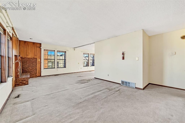 carpeted empty room featuring a textured ceiling, wooden walls, and a brick fireplace