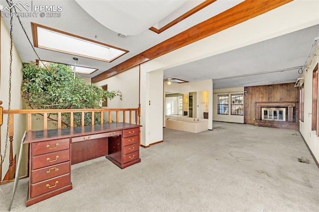 carpeted home office featuring a brick fireplace, ceiling fan, wooden walls, and a skylight