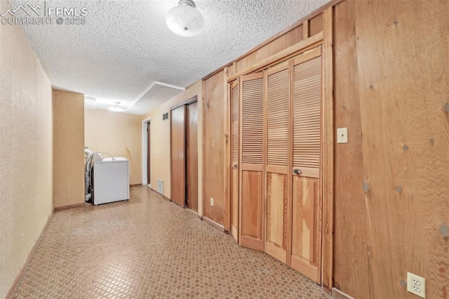 corridor with wood walls, a textured ceiling, and washer / clothes dryer