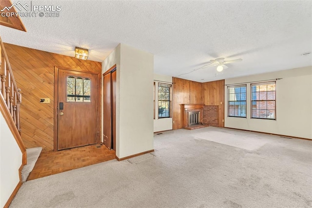 carpeted entryway featuring ceiling fan, a textured ceiling, wooden walls, and a brick fireplace