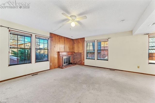 unfurnished living room with wooden walls, a brick fireplace, ceiling fan, a textured ceiling, and light colored carpet