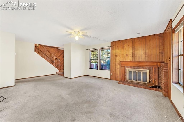 unfurnished living room with ceiling fan, light colored carpet, a fireplace, and wooden walls