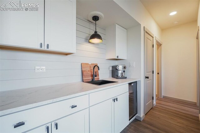 kitchen featuring light stone countertops, dark wood-type flooring, sink, pendant lighting, and white cabinets