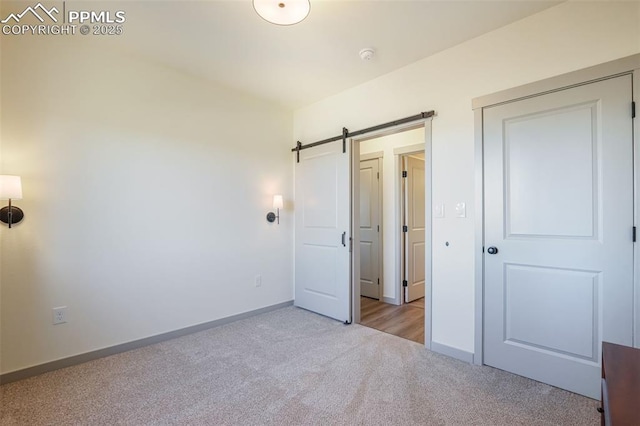 unfurnished bedroom featuring a barn door and light colored carpet