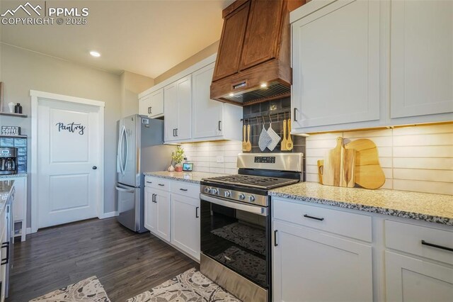 kitchen featuring decorative backsplash, premium range hood, light stone counters, stainless steel appliances, and white cabinetry