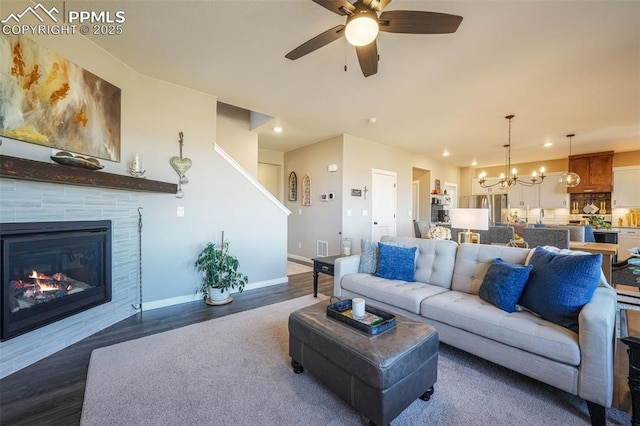 living room with a tile fireplace, ceiling fan with notable chandelier, and dark hardwood / wood-style floors