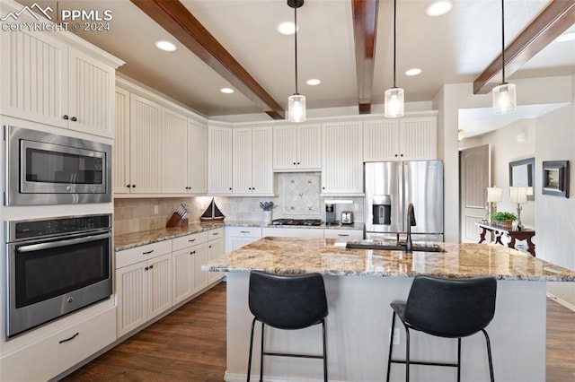 kitchen featuring appliances with stainless steel finishes, dark wood-type flooring, beam ceiling, decorative light fixtures, and an island with sink