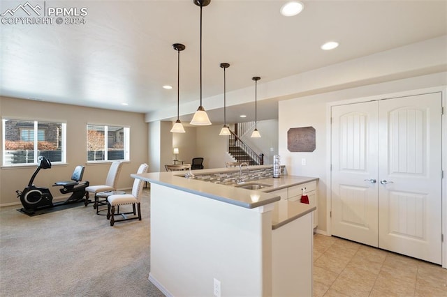 kitchen with kitchen peninsula, light colored carpet, sink, white cabinetry, and hanging light fixtures