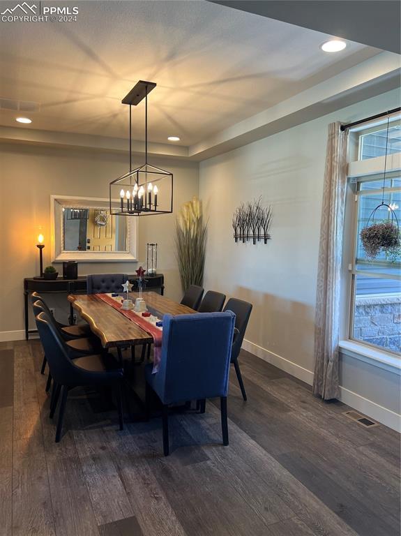 dining area with a notable chandelier, dark hardwood / wood-style flooring, and a raised ceiling