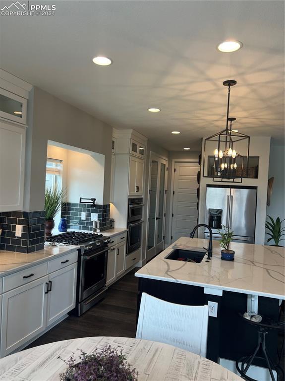 kitchen with appliances with stainless steel finishes, light stone counters, a kitchen island with sink, sink, and white cabinetry