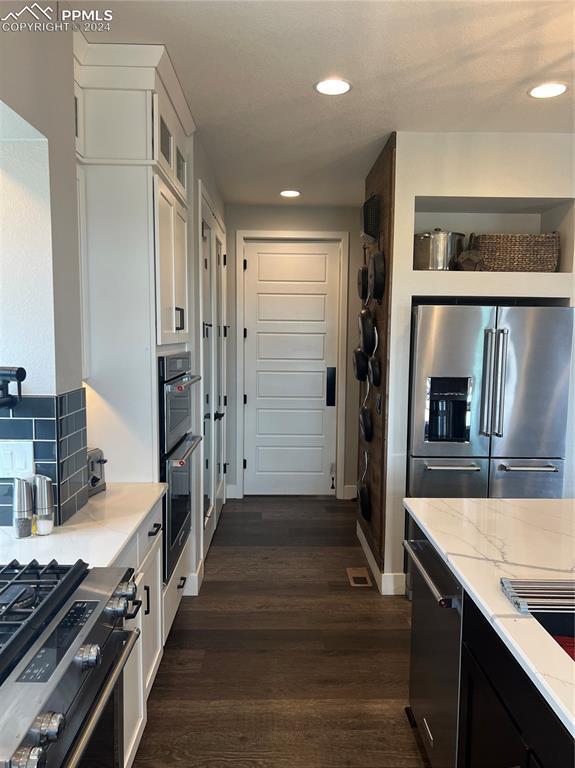 kitchen with dark hardwood / wood-style flooring, stainless steel appliances, white cabinetry, and light stone counters