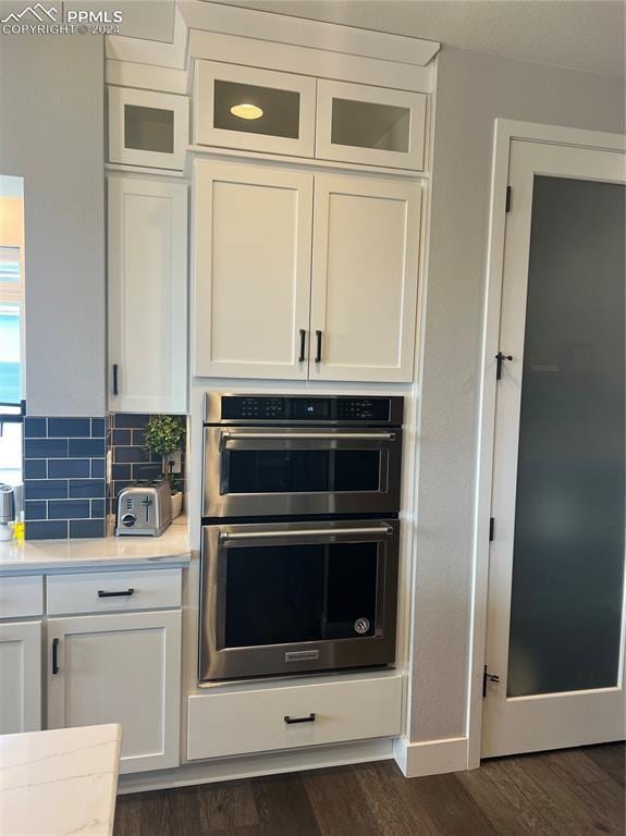 kitchen with tasteful backsplash, white cabinets, stainless steel double oven, and dark hardwood / wood-style floors