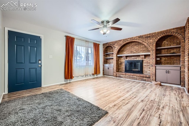 unfurnished living room with hardwood / wood-style flooring, ceiling fan, brick wall, and a brick fireplace