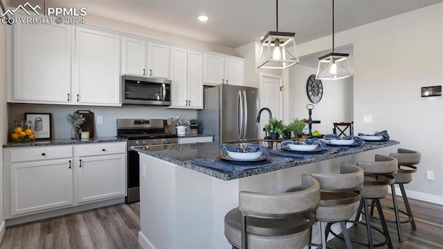 13358 Savannah Falls Ct, Peyton, CO 80831 - kitchen featuring white cabinets, a kitchen bar, dark wood finished floors, a center island with sink, and appliances with stainless steel finishes