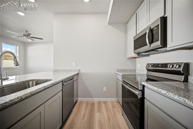 kitchen featuring ceiling fan, sink, stainless steel appliances, light stone counters, and light wood-type flooring