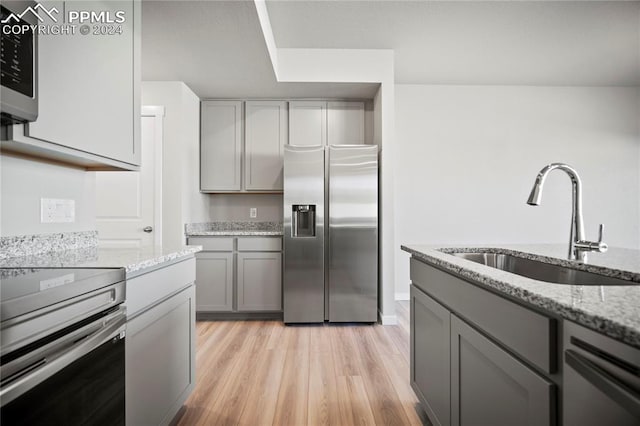 kitchen with gray cabinets, stainless steel appliances, light stone counters, and sink