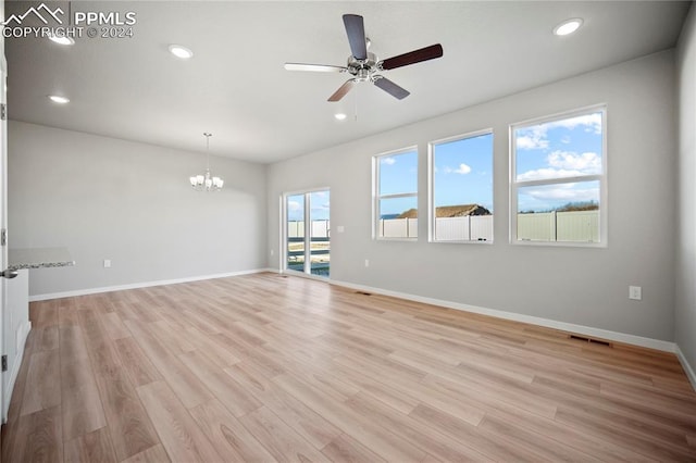 unfurnished room with ceiling fan with notable chandelier, a healthy amount of sunlight, and light hardwood / wood-style flooring